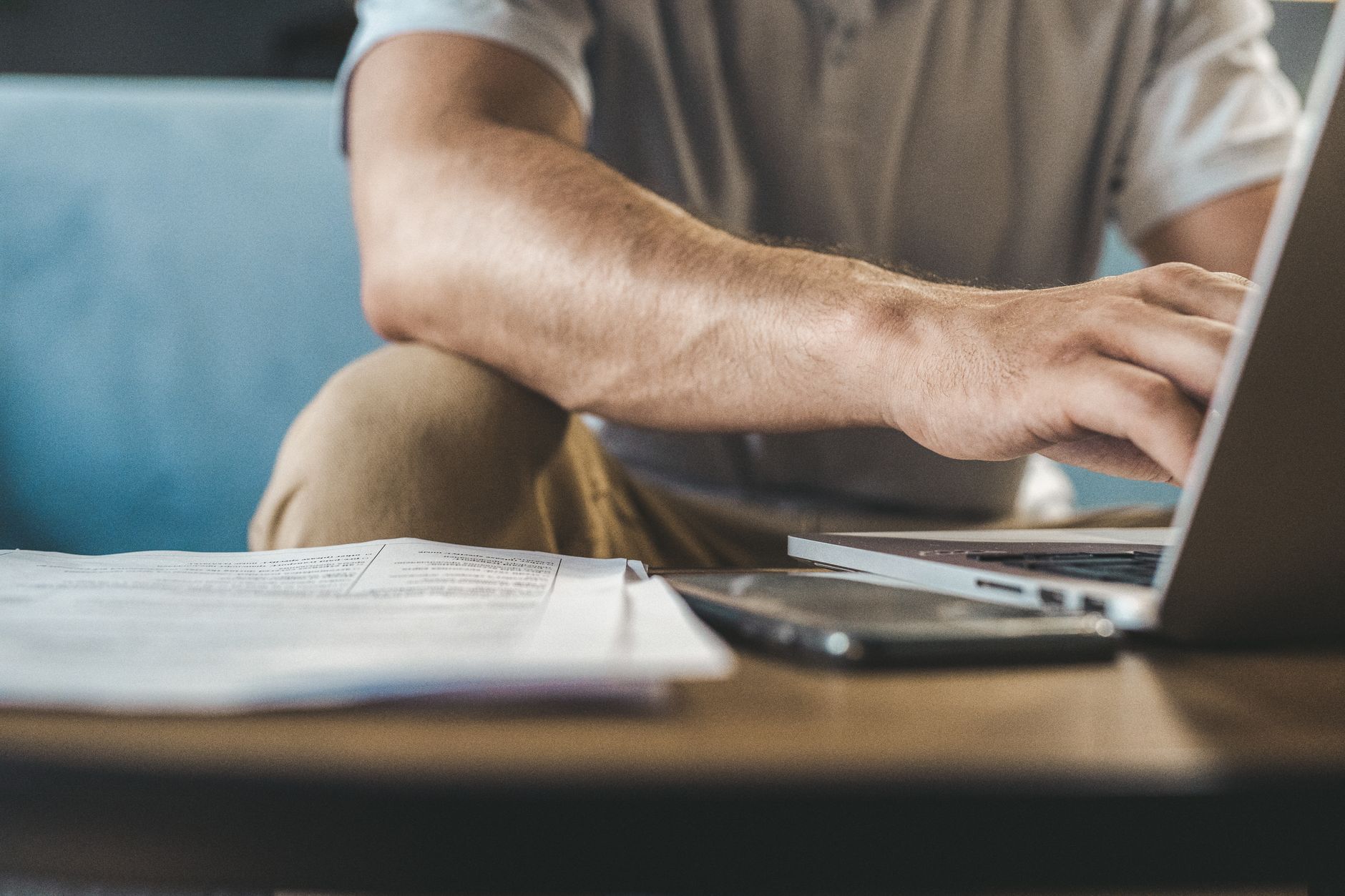 Hands typing on a laptop beside printed documents